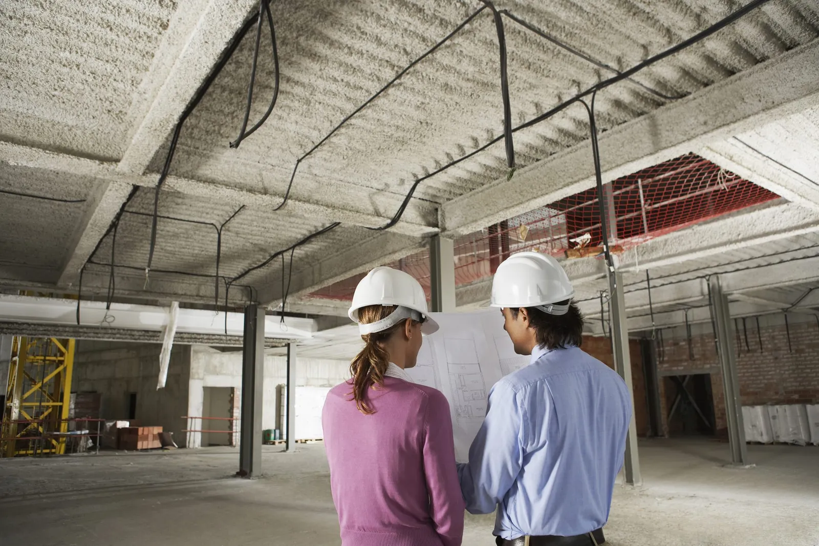 Rear view of architect and construction manager reading blueprint at site